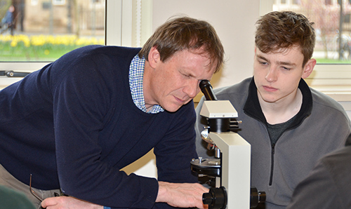 Male teacher looking through a micrsocope with a male student