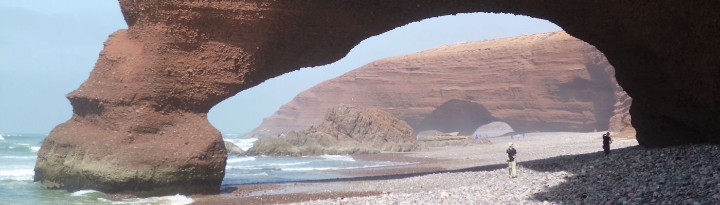 People walking under stone arches on a beach