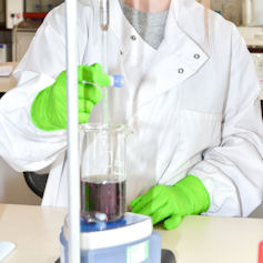 Scientist with white coat and gloves testing liquid sample