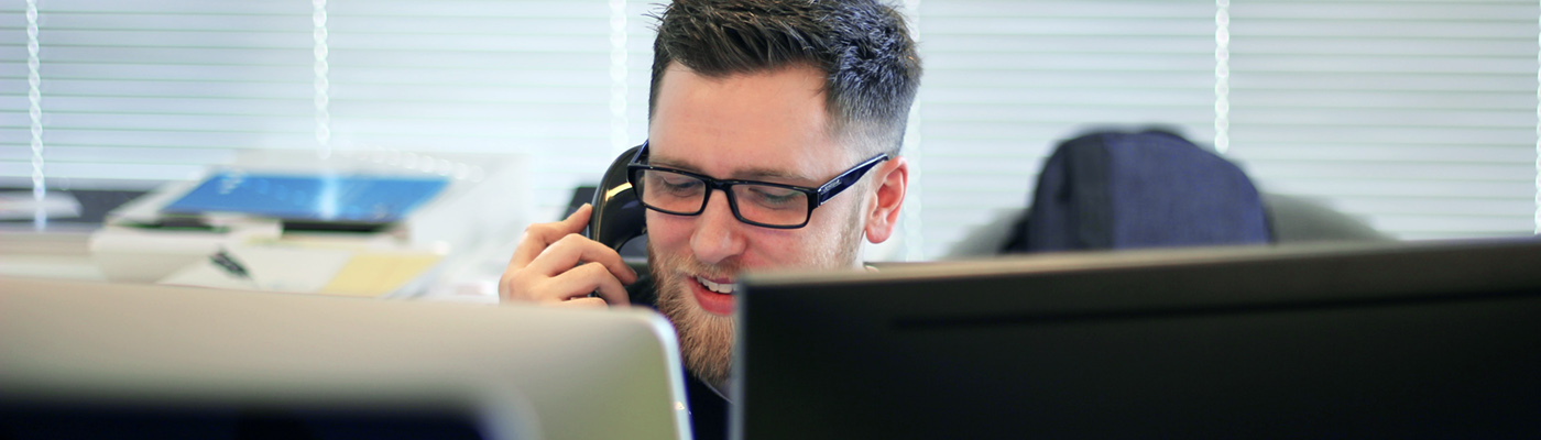 A man sits behind computer screens on the telephone.
