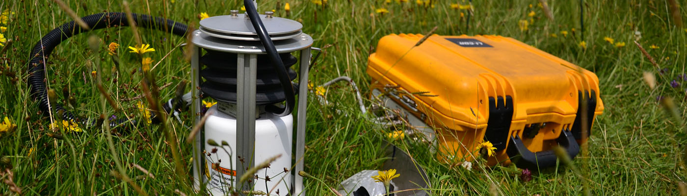 Scientific equipment and a yellow box lay among long grass in a meadow.