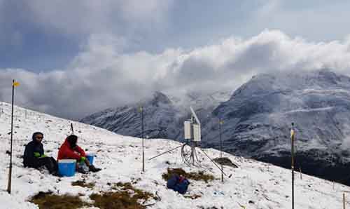 Two people in snow suits sit in snow on a mountain in Austria.