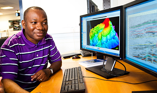 A male student studying data on two computer screens