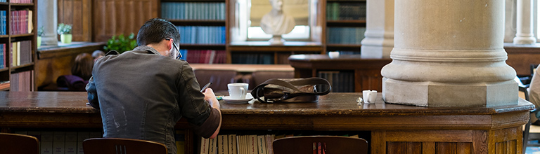 The back of a student working away surrounded by books