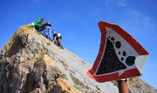 Three people climbing on a rock near a loose rocks warning sign.