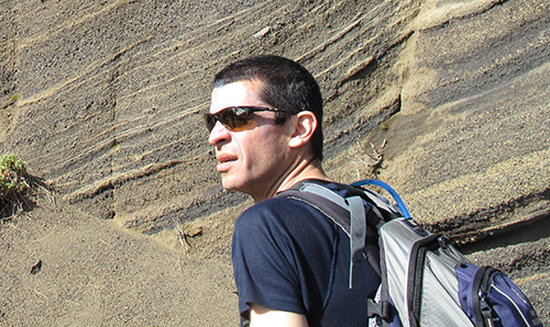 A man in sunglasses peering out in front of a cliff face