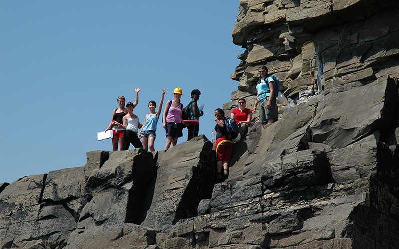 Students waving from a rock face in Pembroke