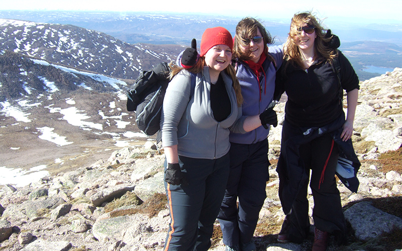 Three female students smiling atop a mountain in Scotland
