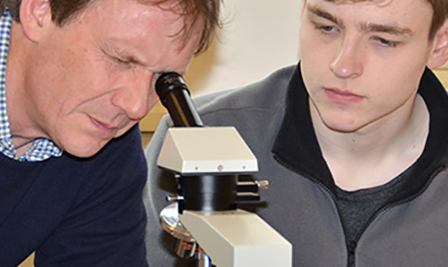 Employer looking through magnifying glass while student looks on