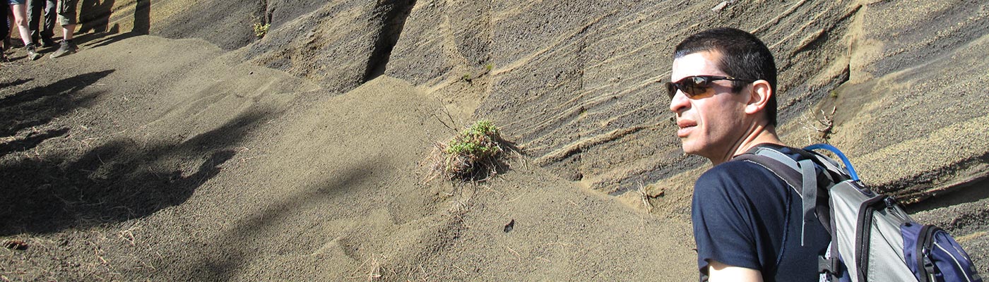 A man in sunglasses peering out in front of a cliff face